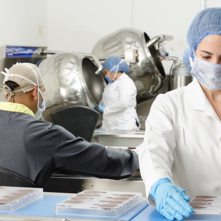 Workers in a food processing facility handling equipment and products, wearing protective gear such as masks, gloves, and hairnets for safety and hygiene. This image illustrates the precision and care in manufacturing processes